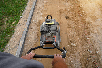 worker rams the ground with a vibrating machine. Top view.