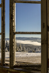 Widok na ośnieżone Karkonosze przez stare, zamrożone okno schroniska. © Tomasz