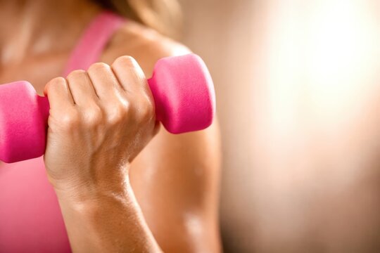 A woman is lifting a pink dumbbell