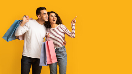 Big Sales. Excited Young Arab Couple Holding Shopping Bags And Pointing Aside At Copy Space On...