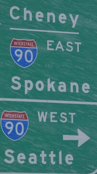 CLOSE UP: Traffic sign weathers a severe blizzard engulfing the state of Washington. Green highway traffic sign directs traffic around the state of Washington during a snowstorm. Extreme weather.
