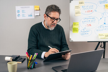 Senior business consultant writing digital notes during strategic analysis