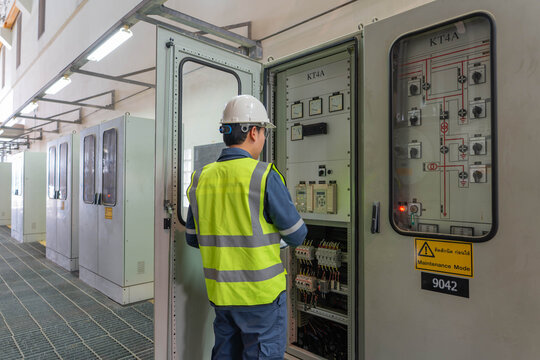 Professional electrical engineer opening indoor control cabinet and switchgear for inspection, monitoring power distribution system and circuit breakers for building energy management.