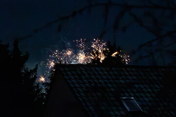 New Years Eve fireworks exploding behind rooftops at night, Silvester 2025