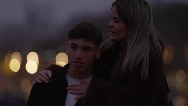 A young couple embraces in Paris at dusk The woman hugs the man who rests his head on her shoulder Bokeh lights create a romantic atmosphere in the background The clip captures a moment of love and af