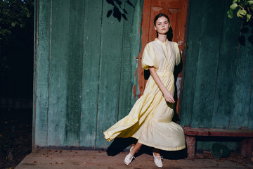 woman dress outdoor portrait vintage wooden sunlight shadow, in yellow standing by rustic door and bench in soft light authentic inclusive