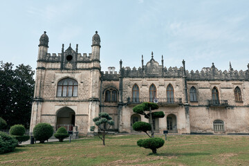 Fototapeta premium historic architecture mansion garden with trimmed topiary and stone facade under overcast sky, authenticity inclusivity