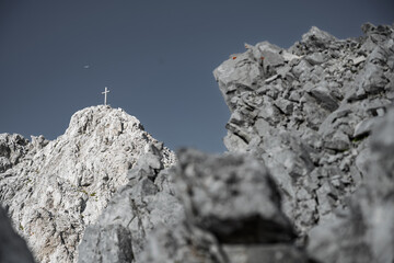 Solitary summit cross towering above surrounding peaks, rarely visited despite stunning views;...