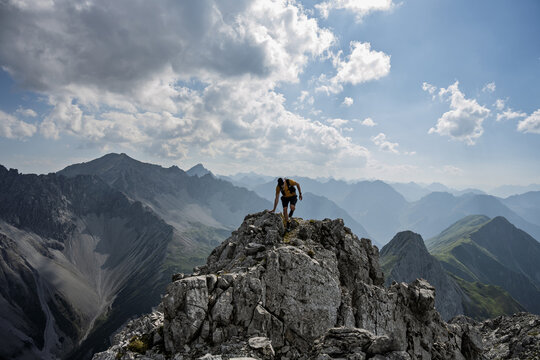 Mountaineer standing on a rocky ridge with breathtaking panoramic view over countless peaks in Tyrol, Austria, dramatic alpine landscape and clear sky. - Powered by Adobe