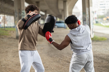 Two men practice their boxing techniques beneath a structural overpass, showcasing dedication and urban athleticism.