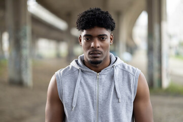 A serious young man stands confidently in an urban setting, embodying strength and determination in this striking portrait.