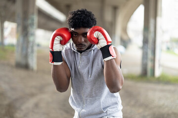 A boxer assumes a defensive stance with gloves raised, showcasing readiness and determination in a gritty urban setting.