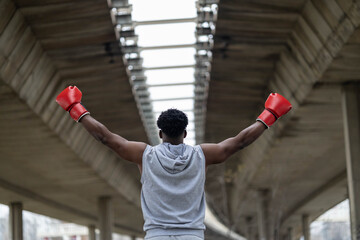 A confident boxer stands with arms raised, exuding strength and focus against a backdrop of concrete, representing achievement.
