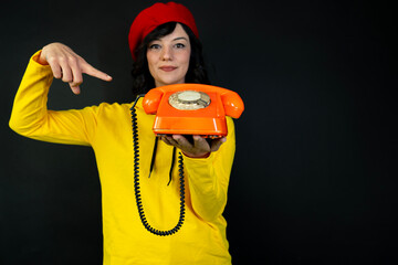 The young woman is holding an antique orange phone and pointing to it. communication concept