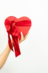 A hand holding a red heart-shaped gift box against a white background.