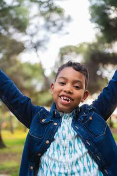 Happy boy smiling with missing front teeth, raising arms in a park setting
