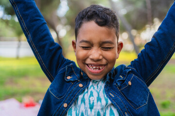 Joyful boy with arms raised, smiling and closing eyes, celebrating happiness in a park
