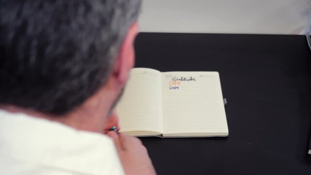 Gratitude List Journals Concept - Gray Haired Middle Aged Man Writes in Journal About What He is Grateful and Thankful For in Life