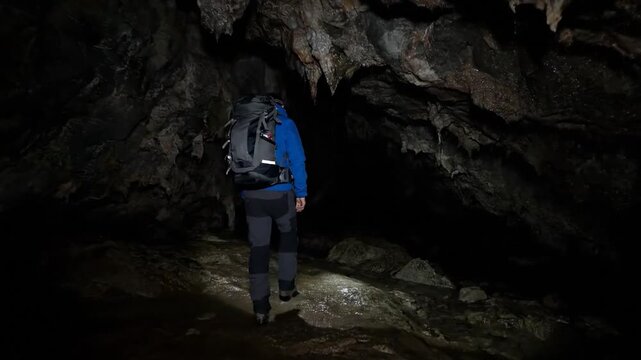 Person with large backpack walks through a dark, damp cave with stalactites