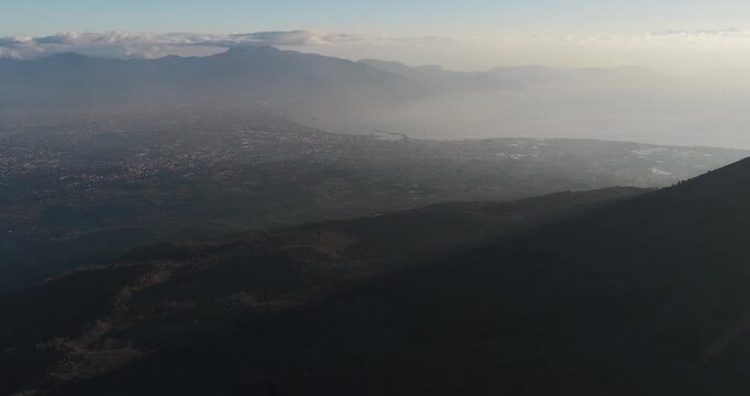 Aerial view of Mount Vesuvius shrouded in a soft haze, casting long shadows over the landscape, Ercolano, Campania, Italy.