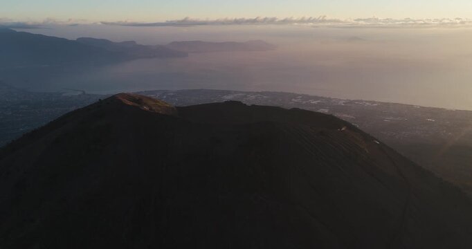 Aerial view of the majestic Mount Vesuvius, a colossal, dark volcano overlooking the serene sea and the distant city lights, Ercolano, Campania, Italy.