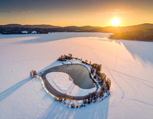 Stunning Aerial View of a Frozen Lake at Golden Sunset Featuring a Unique Circular Island with Snow and Ice in a Serene Winter Landscape