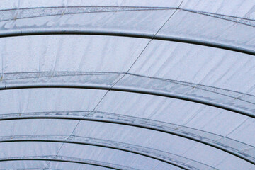 The structure of plastic tunnels (greenhouses) with metal pipes and wires that hold the polyethylene. Wet transparent polyethylene film with droplets of water after rain.