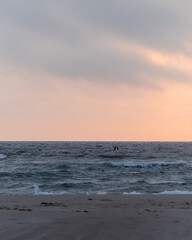 Obraz premium Waves gently crash on a quiet beach at sunset with a soft pink sky and distant figure in the water