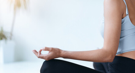 A woman sits in a bright room with natural light entering through a window. She is in a meditative...