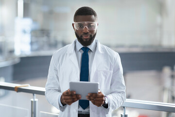 A scientist stands in a laboratory holding a tablet. He wears glasses and a lab coat. The setting is modern with equipment in the background. The scene shows a focus on research and technology.