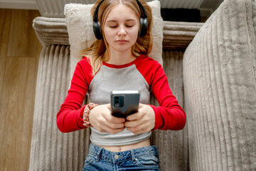 Girl Watching Movie On Smartphone With Headphones While Lying On The Couch