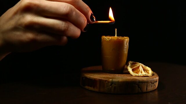 Woman hand lights a match the bees wax candle on wooden candlestick for mood, relaxation, meditation dark black background. Person lighting the decoration handmade single candle flame