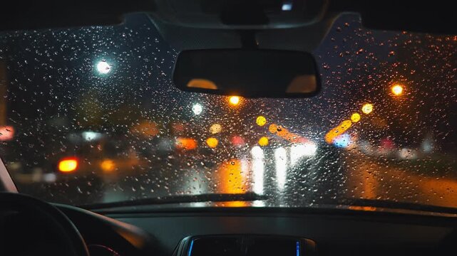 Nighttime car interior view through rain-speckled windshield with blurred city lights