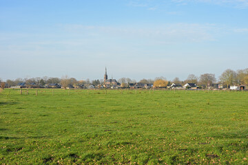 A wide, peaceful view across green pastures toward the church of Loon op Zand, captured from Huis ter Heide nature reserve during a clear day in late December.