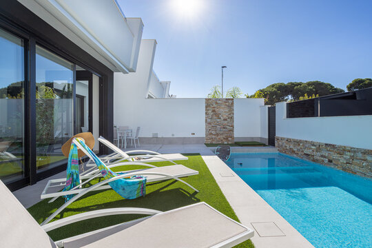 Sunny backyard with pool, loungers and stone wall in modern residential villa