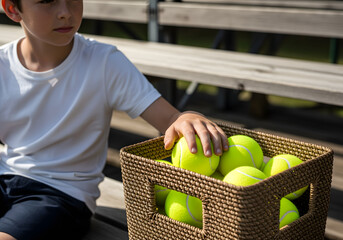 Ball boy with basket collecting tennis balls on court