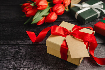 Gift box with red ribbon and fresh red tulip flowers. Easter or birthday holiday black background.
