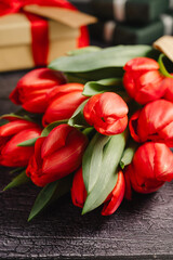 Red tulip bouquet with gift boxes. Easter or birthday holiday black background.