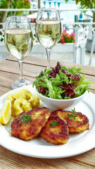 A delicious lunch of crispy fried pork cutlets and egg noodles on a restaurant terrace. Two glasses of white wine complete the perfect summer meal.