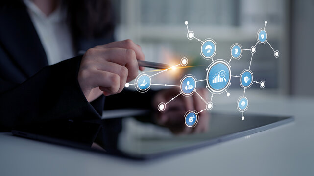 A business professional interacts with a tablet displaying digital icons, symbolizing technology, data analysis, and networking in a contemporary office environment. Tessel - Powered by Adobe