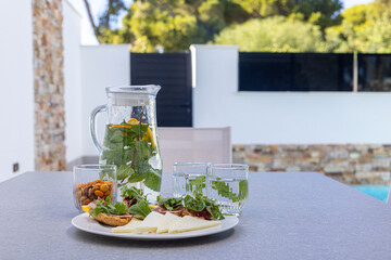 Refreshing outdoor snack setup with infused water, cheese platter, and nuts on modern patio table
