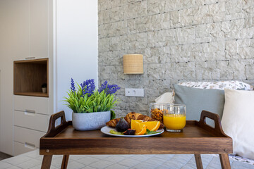 Breakfast tray on bed with orange juice, croissants, figs, and decorative plant in cozy bedroom