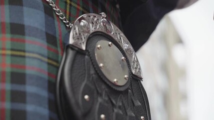 a person wearing tartan playing bag pipes and moving his sporran to the beat.