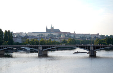 Fototapeta premium Wide river view with arched bridge and distant historic skyline on the horizon, calm water reflections and soft daylight. Peaceful city panorama with travel and urban landscape mood.