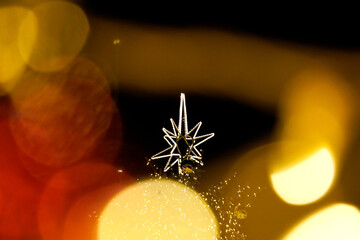 Small metallic star ornament isolated against warm glowing bokeh lights, shallow depth of field and...