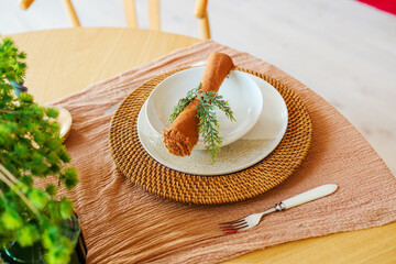 Elegant table setting with white plates, rattan charger, rustic napkin, green sprig, and fork.