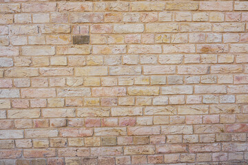 Fototapeta premium Warm textured brick wall background with varied pale yellow and pinkish tones and visible mortar.