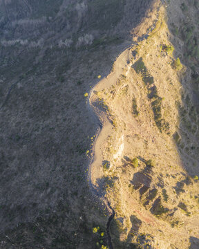 Aerial view of the rugged, sun-kissed Sentiero del Gran Cono, a serpentine trail winding through the Vesuvius National Park's volcanic landscape, Ercolano, Campania, Italy.