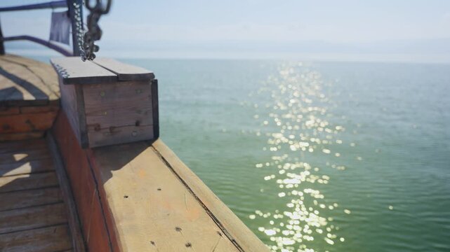 Bow of rustic wooden boat on bright sunny day in Sea of Galilee in Israel. Perspective from deck looking out to lake water as sunlight reflects off its surface. Religious pilgrim guided boat tour ride