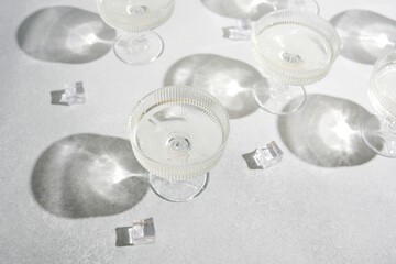 Clear glasses filled with liquid and ice cubes casting shadows on a textured surface.